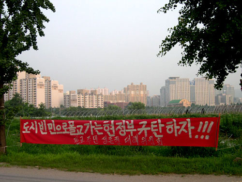 동판교 곳곳에 정부규탄 프래카드가 걸려있다.뒤쪽에 분당 신도시 지역의 아파트가 보인다. 